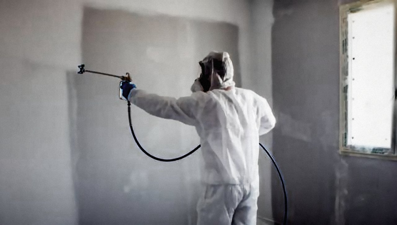 Pintor con equipo airless aplicando pintura en un muro interior